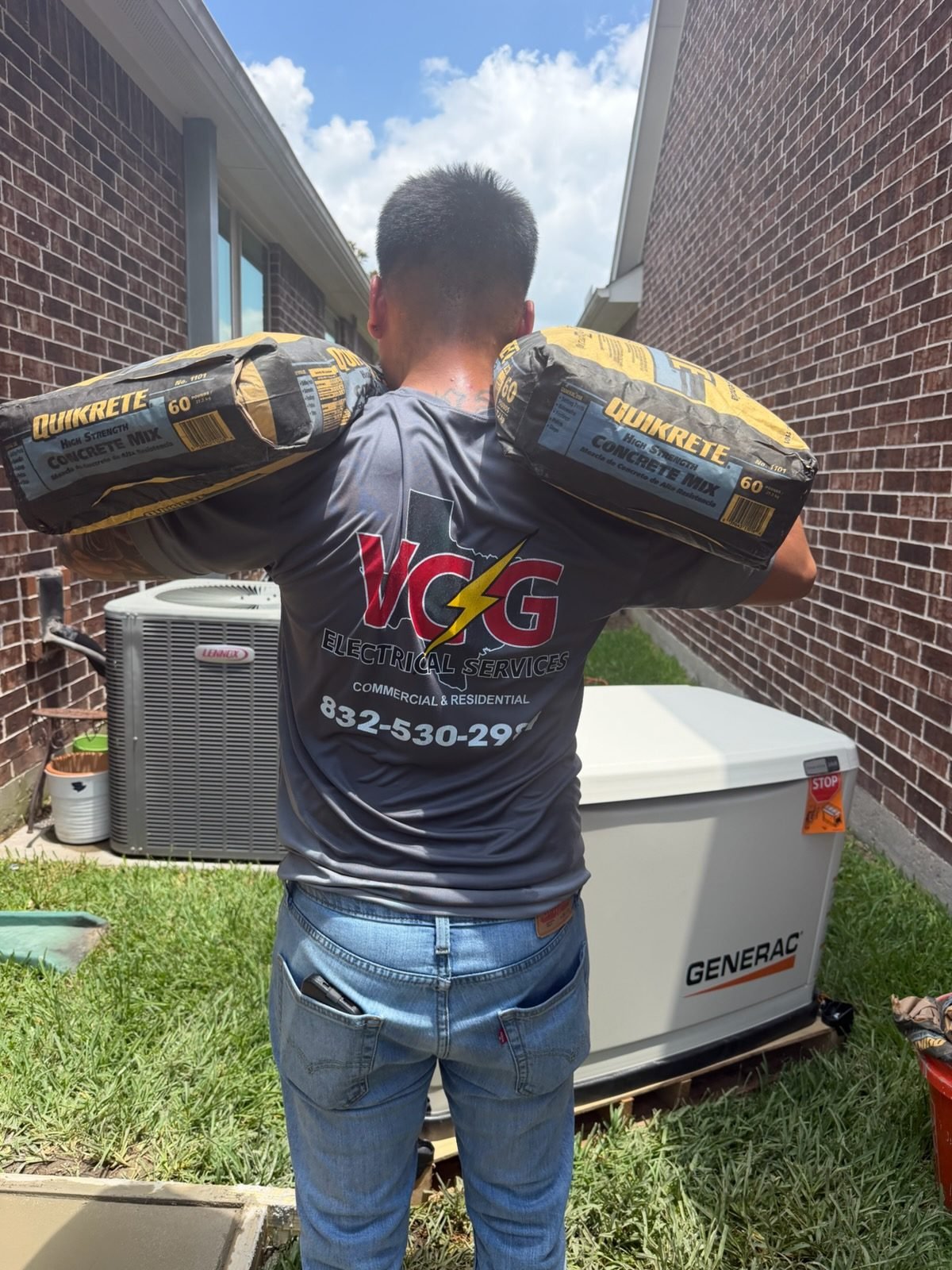 VCG Electrical crew member in a branded uniform carrying concrete mix beside a Generac standby generator in Houston