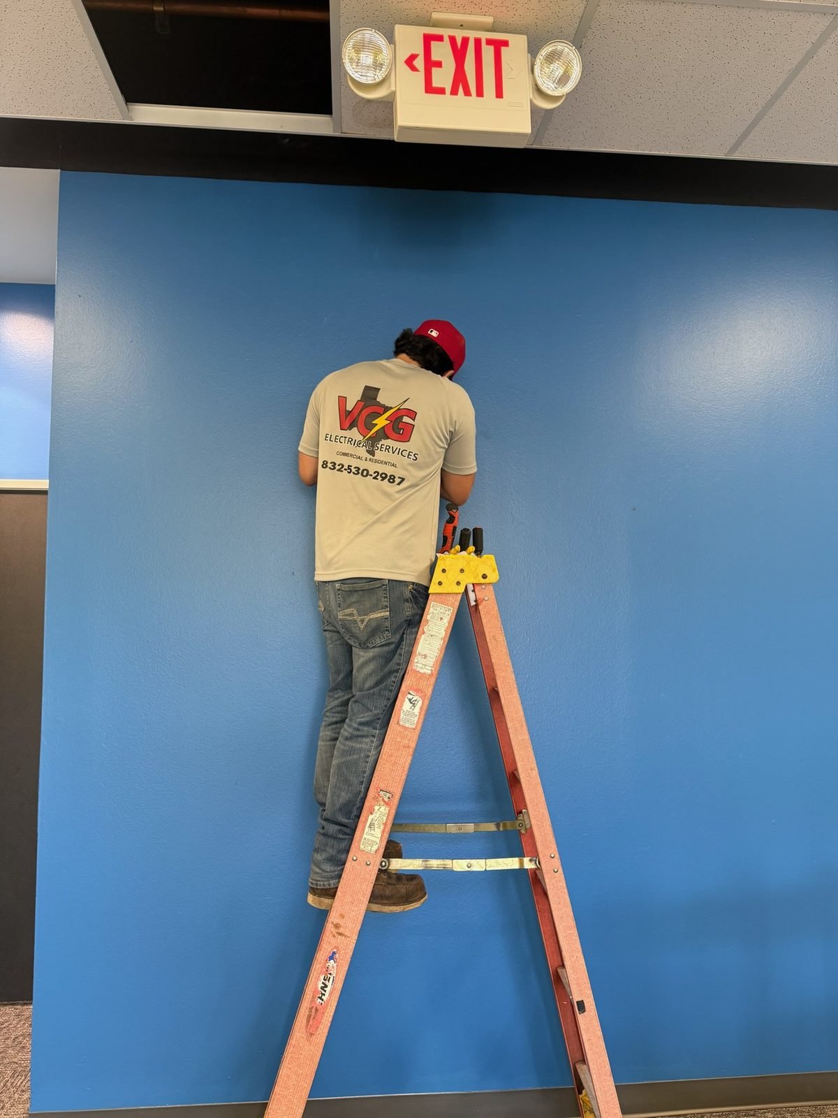 VCG Electrical technician installing commercial emergency exit lighting in a Houston office